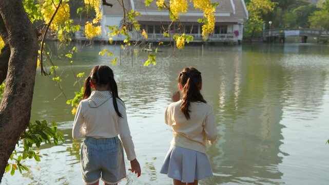 Two Young Thai Girls Feeding Fish at Lumpini Park Lake in Bangkok