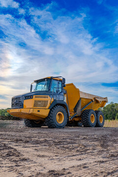 Large yellow articulated dump truck parked on a dirt construction site under a blue sky, USA.