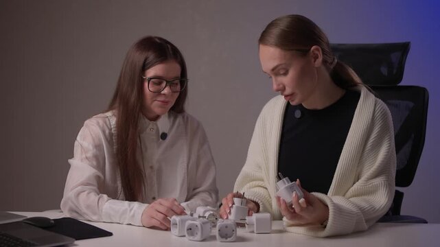 Caucasian women assess smart socket functionality carefully. Two ladies of Caucasian descent collaboratively inspect and compare smart socket models on studio desk