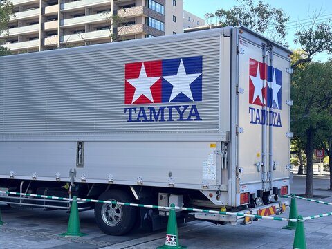 Tamiya Inc. branded logistics box truck with blue and red star logos parked on an urban street near residential buildings for a model hobby event - Shizuoka, Japan, October 15, 2023