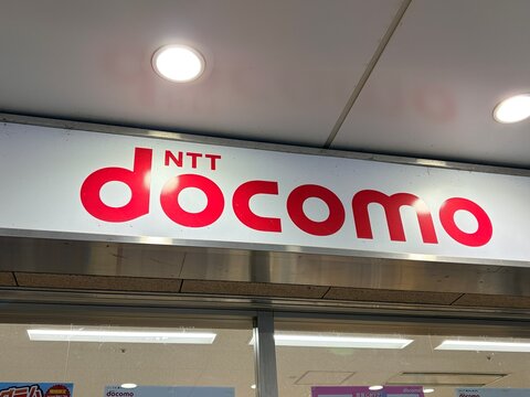 NTT Docomo brand logo on an illuminated storefront sign at a mobile phone retail shop featuring distinctive red typography in an urban shopping mall - Osaka, Japan, October 15, 2023