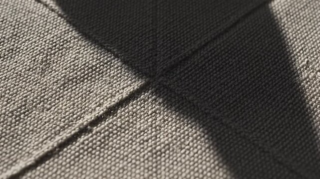 Close-up of textured beige fabric with stitched diamond pattern and dramatic shadow detailed macro shot