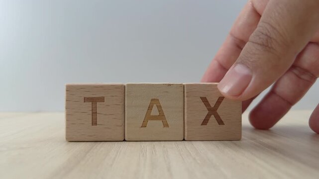 Close up of a hand placing a wooden block with the letter X next to T and A to spell the word TAX on a wooden surface, Concept of financial planning, taxation and accounting