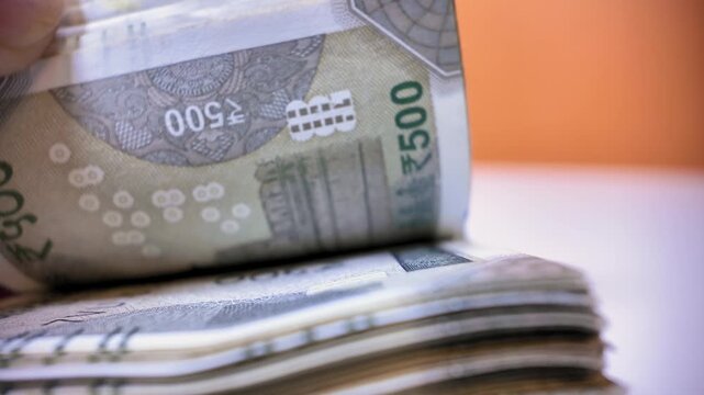 Person counting a large stack of indian 500 rupee banknotes