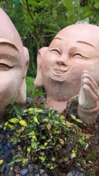 Two playful stone statues of monks share a secret giggle in a lush garden in Ba Na Hills, Da Nang, Vietnam. The statues depict joy and camaraderie.