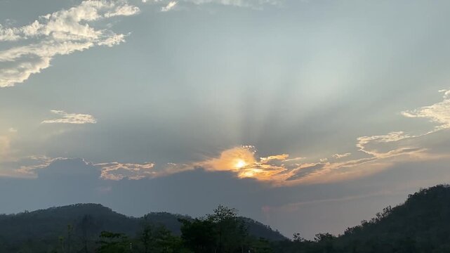 Dramatic crepuscular sun rays beaming through clouds over mountain silhouette at sunset
