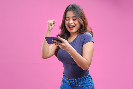 Excited young Asian girl is watching streaming video or playing game on her smartphone.