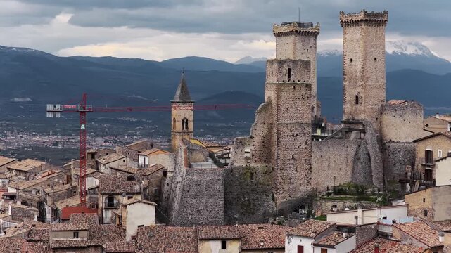 Aerial view of the medieval Caldora Castle with its tall stone towers overlooking the historic rooftops and surrounding mountains in Pacentro, Abruzzo, Italy.