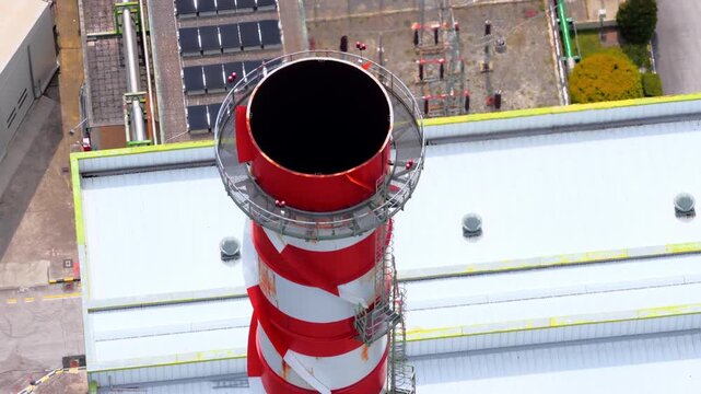 Aerial view of a red and white striped industrial chimney with a metal platform and solar panels on a nearby roof in Bussi sul Tirino, Abruzzo, Italy.
