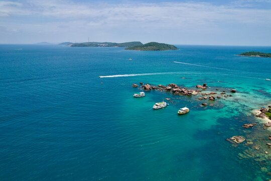 Stunning aerial drone video of Gam Ghi Island on Phu Quoc in south Vietnam with turquoise blue water and vivid coral reefs with tourists snorkeling and jumping off the boats on a hot sunny day