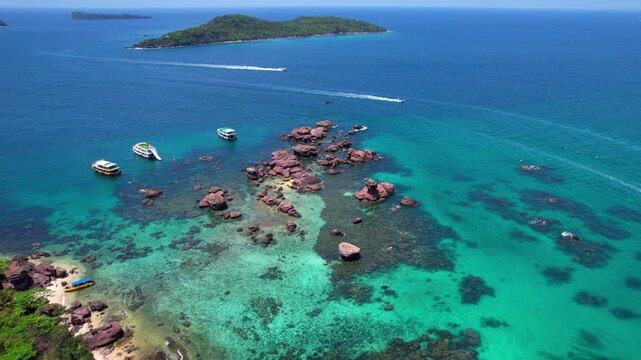 Stunning aerial drone video of Gam Ghi Island on Phu Quoc in south Vietnam with turquoise blue water and vivid coral reefs with tourists snorkeling and jumping off the boats on a hot sunny day