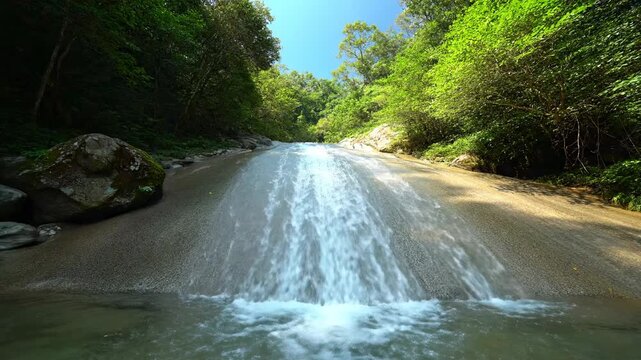 A waterfall cascading over a smooth rock surface, surrounded by lush green foliage