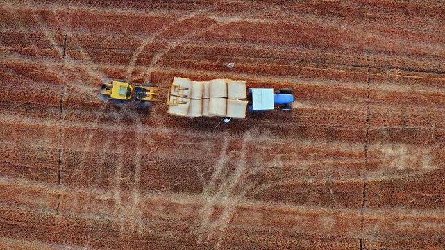 Top down view of modern agricultural machinery harvesting and transporting round hay bales in autumn field