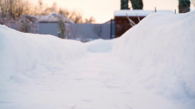 Cleared snow path between tall snowdrifts in rural backyard at sunrise