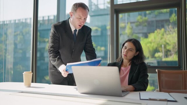 Unhappy boss confronting an employee in a tense workplace discussion about performance, with a modern high-rise office view in the background