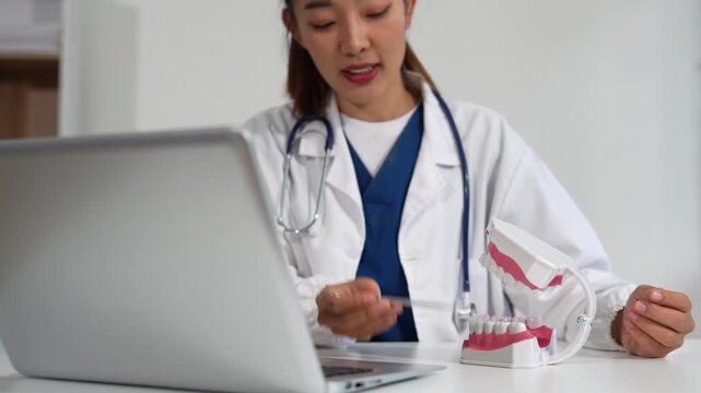 dentist video consultation, communicates with patient via an online conference, uses laptop, diagnoses, recommended and tooth models and analyzing dental treatments, and also answers questions.