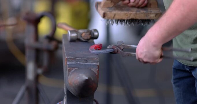 Close-up of a blacksmith using a hammer and punch to shape a metal horseshoe on a steel anvil within a traditional workshop setting.