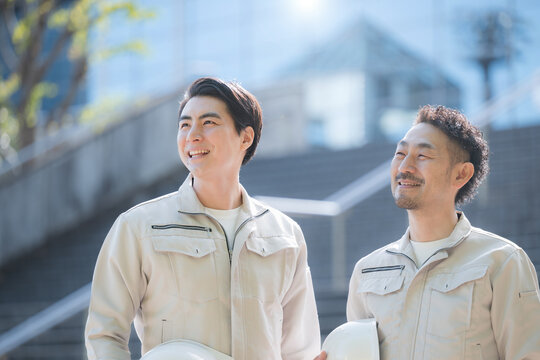 ヘルメットを持つ作業員のポートレート メンテナンスやゼネコンのような建設現場と成長、ビル背景で見上げる作業着の2人