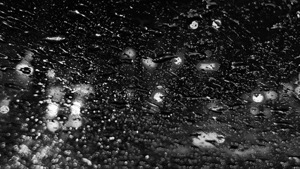 Obraz premium Monochrome abstract texture of raindrops on glass with dramatic night city bokeh