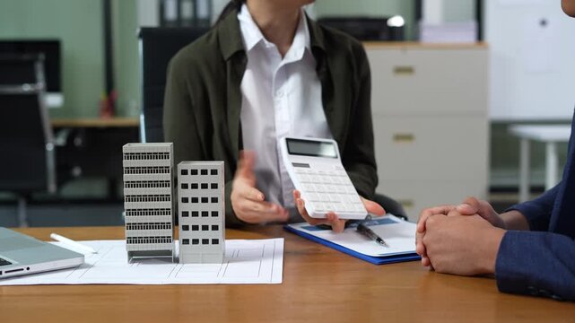 Home loan officer uses a calculator to calculate with a house plan.