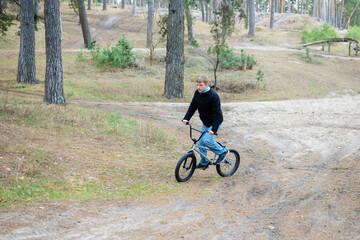 Naklejka premium Teenage Boy Riding BMX Bike on Dirt Trail in Pine Forest Outdoor Activity and Extreme Sport