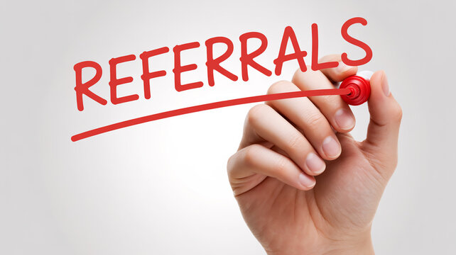 A hand writing referrals with a red marker pen up close.