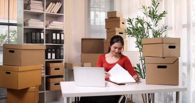 Woman working, online shop owner checking orders from websites on the internet to confirm orders with customers who have ordered them and packing them for delivery. Concept of selling products online.