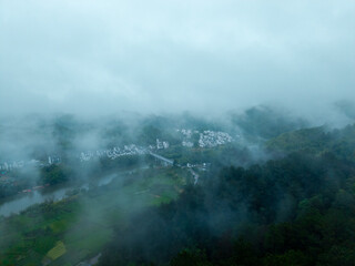 Fototapeta premium A high angle view captures the ancient Huizhou City located in She County of Anhui Province in China as it sits surrounded by green mountains and thick morning fog during the day