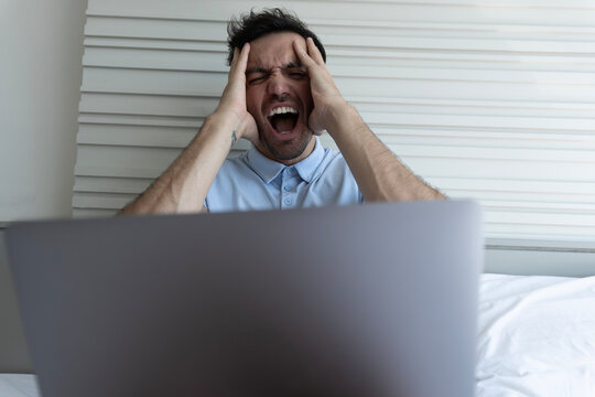 Close-up of an angry man with his hand on his head reacting intensely to his laptop.