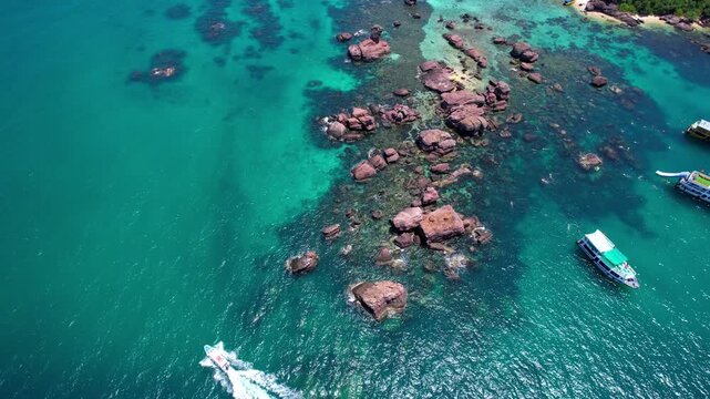 Stunning aerial drone video of Gam Ghi Island on Phu Quoc in south Vietnam with turquoise blue water and vivid coral reefs with tourists snorkeling and jumping off the boats on a hot sunny day