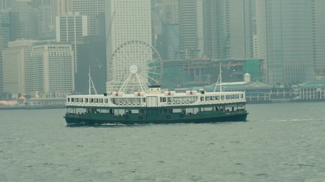 Star Ferry Crossing Victoria Harbour with Hong Kong Skyline and Ferris Wheel in Haze