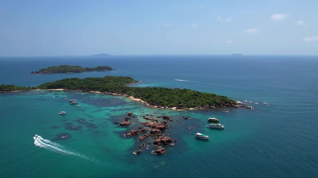 Stunning aerial drone video of Gam Ghi Island on Phu Quoc in south Vietnam with turquoise blue water and vivid coral reefs with tourists snorkeling and jumping off the boats on a hot sunny day