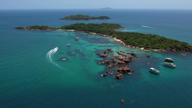 Stunning aerial drone video of Gam Ghi Island on Phu Quoc in south Vietnam with turquoise blue water and vivid coral reefs with tourists snorkeling and jumping off the boats on a hot sunny day
