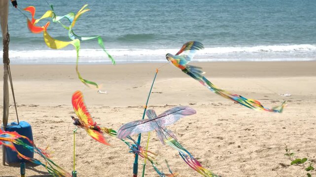 Colorful pinwheel toys in the shape of parrots and butterflies spinning in the wind displayed for sale on a tropical beach. Street trade concept