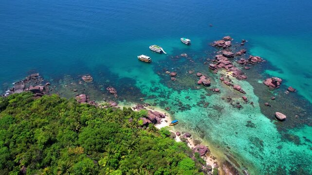 Stunning aerial drone video of Gam Ghi Island on Phu Quoc in south Vietnam with turquoise blue water and vivid coral reefs with tourists snorkeling and jumping off the boats on a hot sunny day