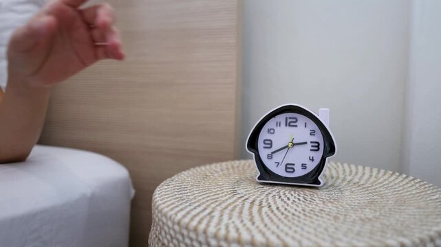 Hand Reaching to Turn Off Alarm Clock on Bedside Table