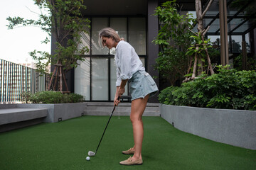 Naklejka premium Woman putting golf ball on private green in modern residential courtyard