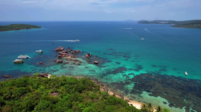Stunning aerial drone video of Gam Ghi Island on Phu Quoc in south Vietnam with turquoise blue water and vivid coral reefs with tourists snorkeling and jumping off the boats on a hot sunny day