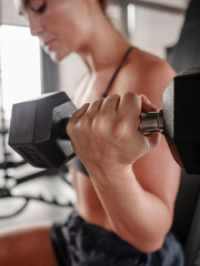 Obraz premium Athletic woman performing seated dumbbell bicep curl on incline bench in modern gym