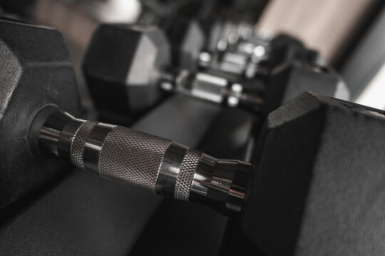 Close-up and row of black hex dumbbells on rack in modern gym
