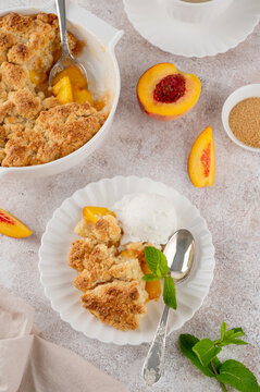 Homemade summer peach cobbler. Pie with juicy peaches, a scoop of vanilla ice cream and fresh mint on a white plate. Comfort food.