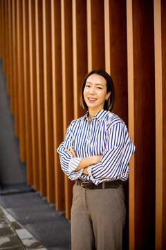 Woman stands by wooden wall in urban setting with casual outfit and friendly smile
