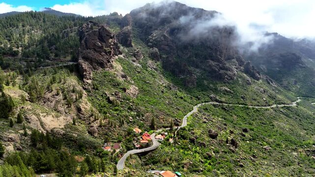 Aerial view of Caminito Roque Nublo winding through the rugged mountains and lush green slopes near the village of La Culata, Canarias, Spain.
