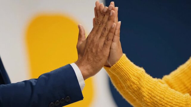 Close-up of coworkers giving a high-five in slow motion with bright yellow and navy colors