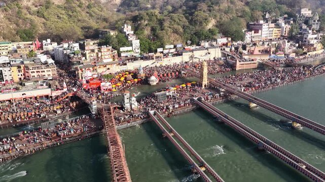 A cinematic aerial tracking shot of Har Ki Pauri in Haridwar. The camera performs a smooth forward push-in, transitioning from a wide panoramic view of pilgrim crowd at the place.