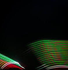 Obraz premium Long exposure light painting featuring vibrant red and green wavy lines flowing across a dark black background.