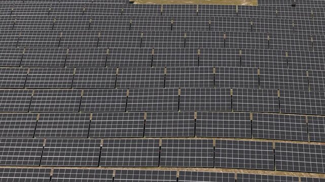 Aerial view of a large array of photovoltaic solar panels installed on open ground under bright daylight in Palmela, Setubal, Portugal.