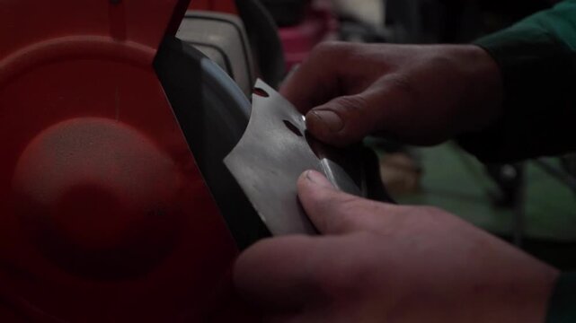 Worker Sharpening Blade with Electric Grinder Close Up. Worker sharpening metal blade with electric bench grinder