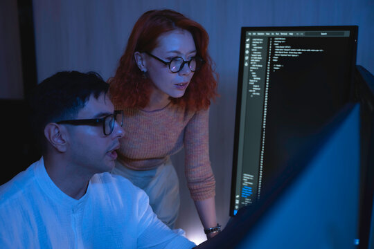 Two software developers collaborating at night, focusing on code review and debugging process on a computer screen, representing teamwork, innovation, and modern software development workflow.