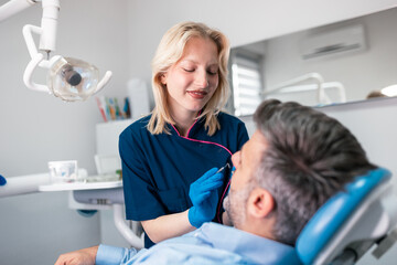 Obraz premium Young female dentist examining male patient's teeth in clinic Professional dental care, oral hygiene, and healthcare concept. Woman doctor using dental tools for checkup in modern medical office space
